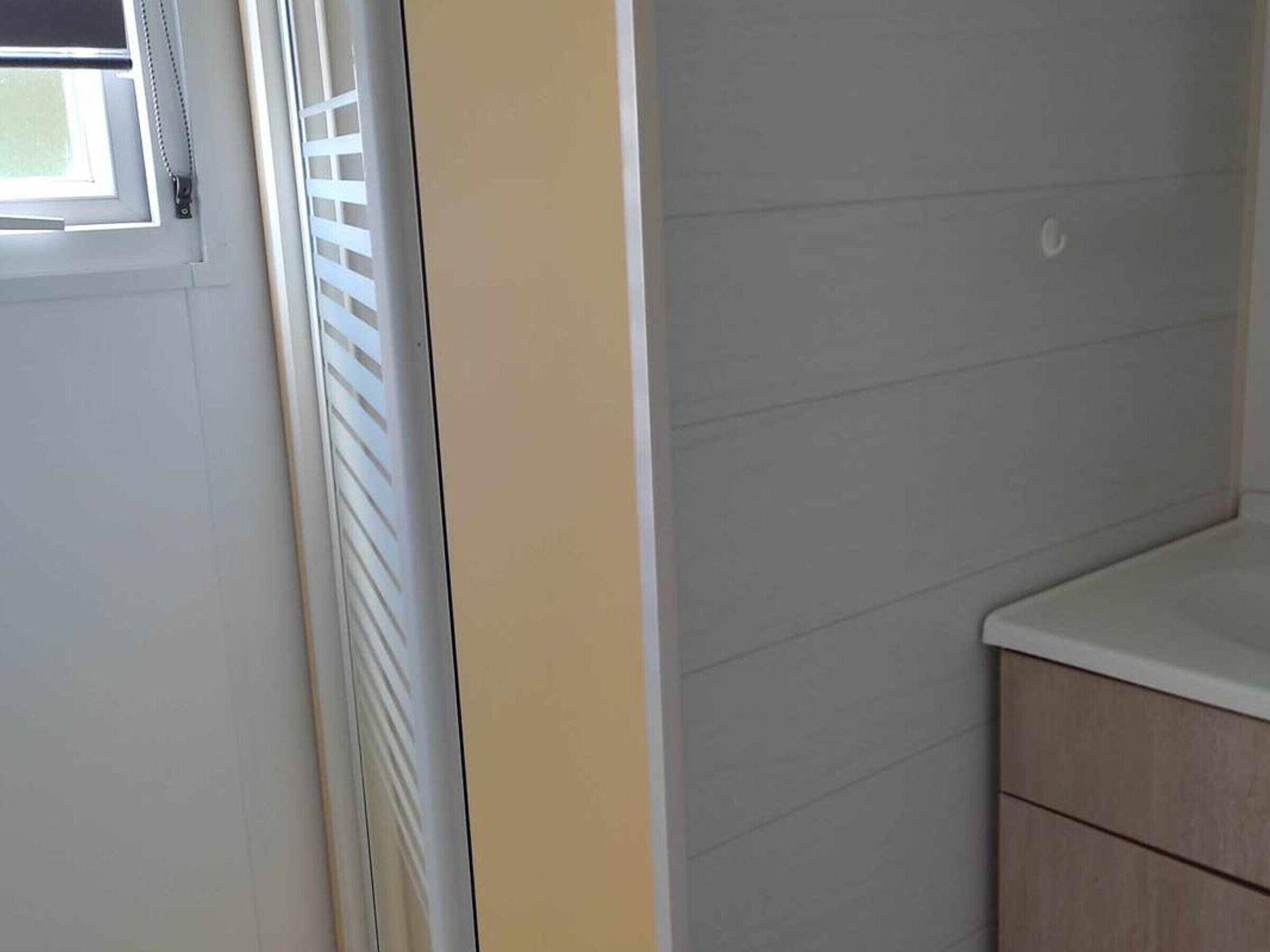 Un baño con una puerta blanca, una ventana con persianas y un armario de madera.