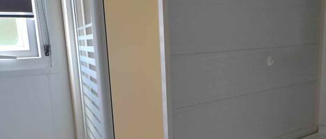 Un baño con una puerta blanca, una ventana con persianas y un armario de madera.