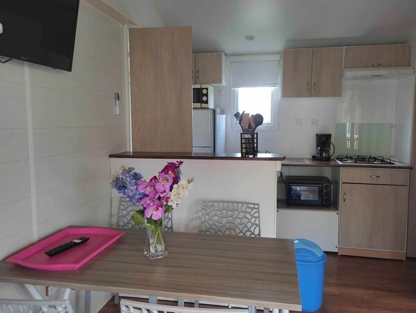 A compact kitchen with wooden cabinets, a gas stove, a microwave, and a coffee maker. - 32m² Mobile Home with Terrace for 4 People in Anduze (Anduze)