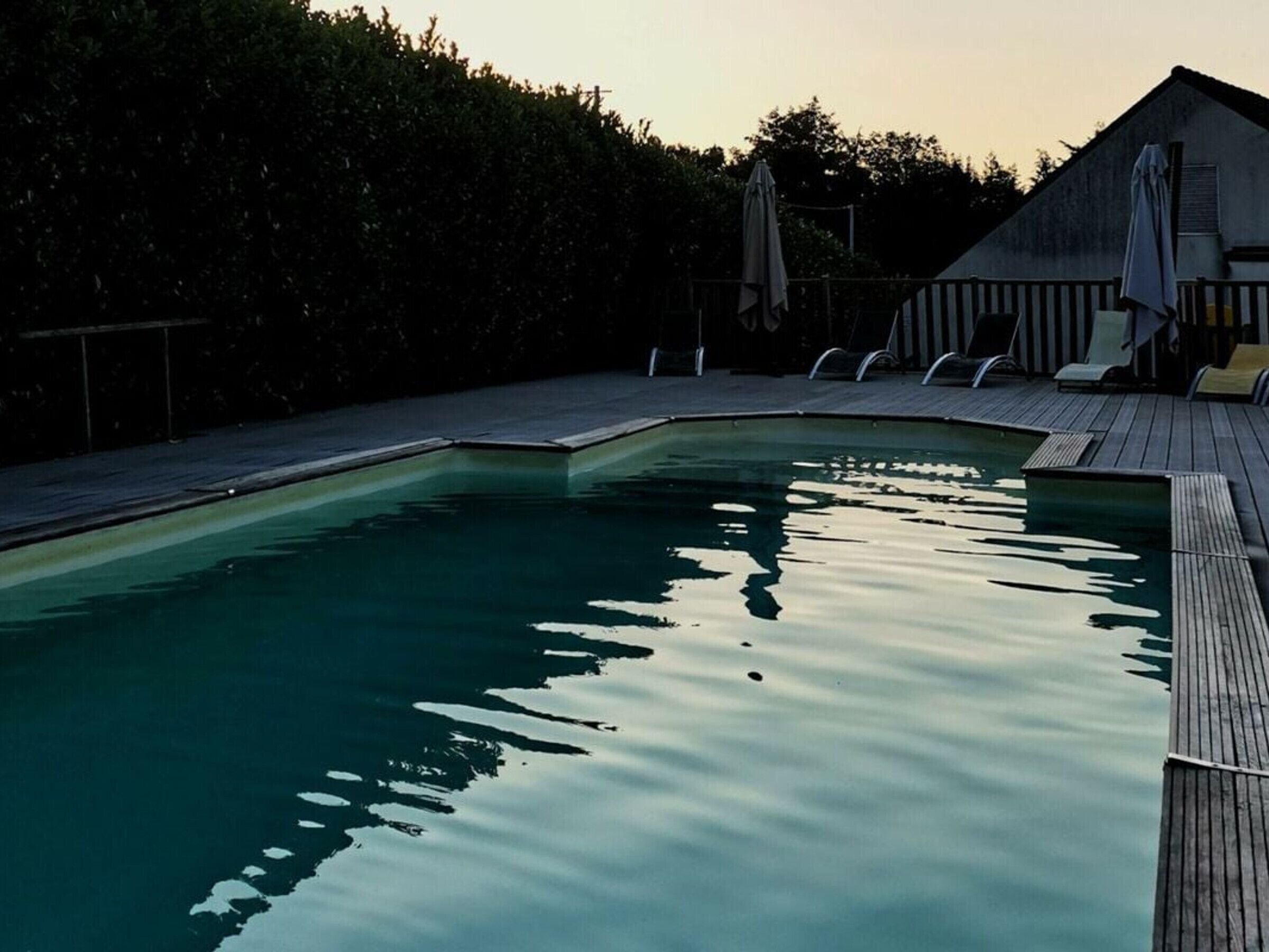 A swimming pool with a wooden deck and lounge chairs.