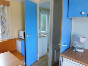 A compact room with a kitchenette, a small bathroom, and a bed. - Mobile home with terrace for 4 people (Guégon)