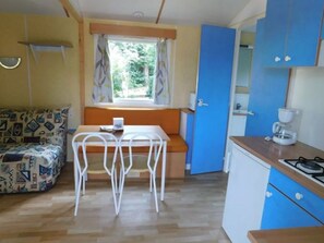 A compact room with a kitchenette, a dining area with a table and chairs, and a sofa with a patterned cover. - Mobile home with terrace for 4 people (Guégon)
