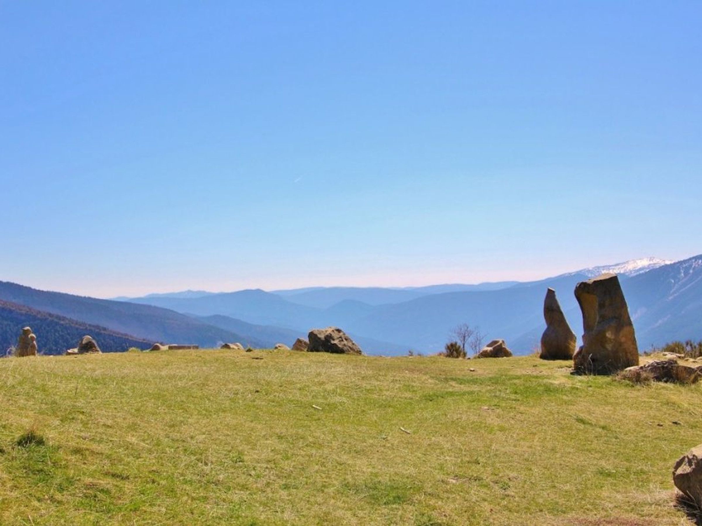 A grassy field with large boulders and distant mountains under a clear sky.