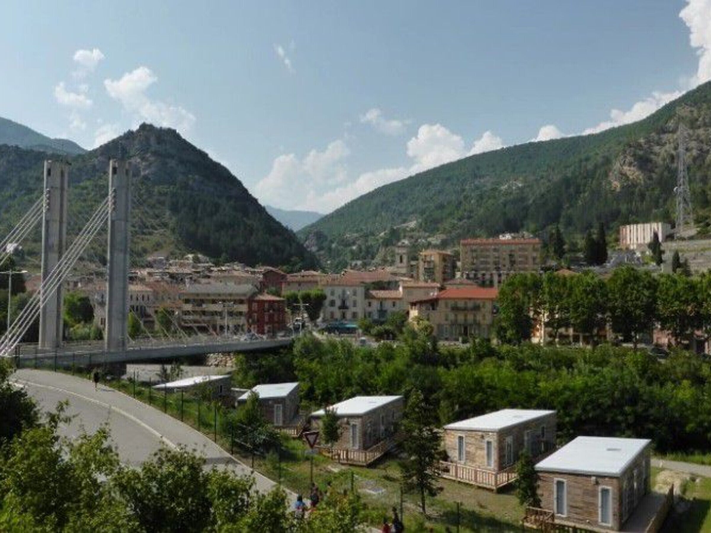 Un pont enjambant une rivière, avec des bâtiments et de la végétation en arrière-plan.