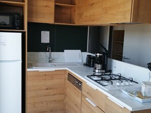 Eine moderne Küche mit Holzausstattung, einer weißen Arbeitsplatte, einer Spüle aus Edelstahl, einem Herd und einer Mikrowelle.