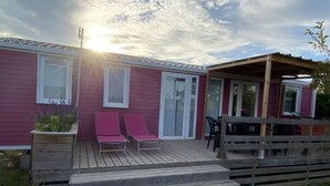 Uma casa térrea com um deck de madeira, duas poltronas cor-de-rosa e uma área de varanda coberta.