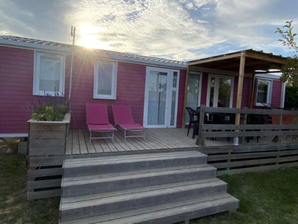 Einbungalow mit Holzterrasse, zwei rosa Liegestühlen und einer überdachten Terrasse.