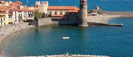 Une ville côtière dotée d’une tour imposante, d’une plage de sable et d’un port de plaisance où sont amarrés des bateaux.