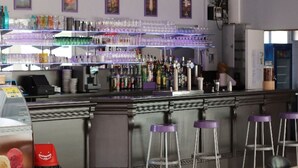 En bar med disk, barstole og hylder fyldt med flasker og glas.