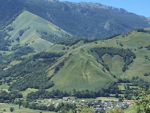 A rural landscape with rolling hills, a small village, and a mountain range in the background.