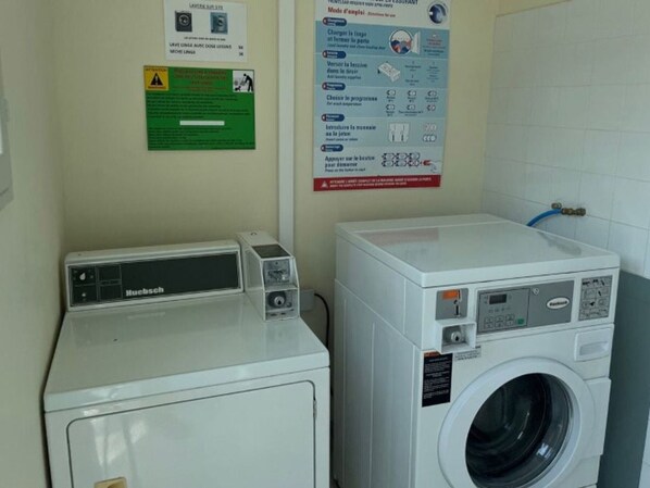A laundry area with a front-loading washing machine and a top-loading dryer. There are instructional posters on the wall.