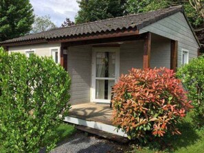 A small, single-story building with a porch and a door, surrounded by greenery.