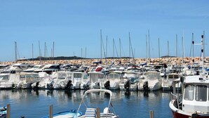 Un puerto deportivo con barcos amarrados, agua tranquila y una costa rocosa al fondo.