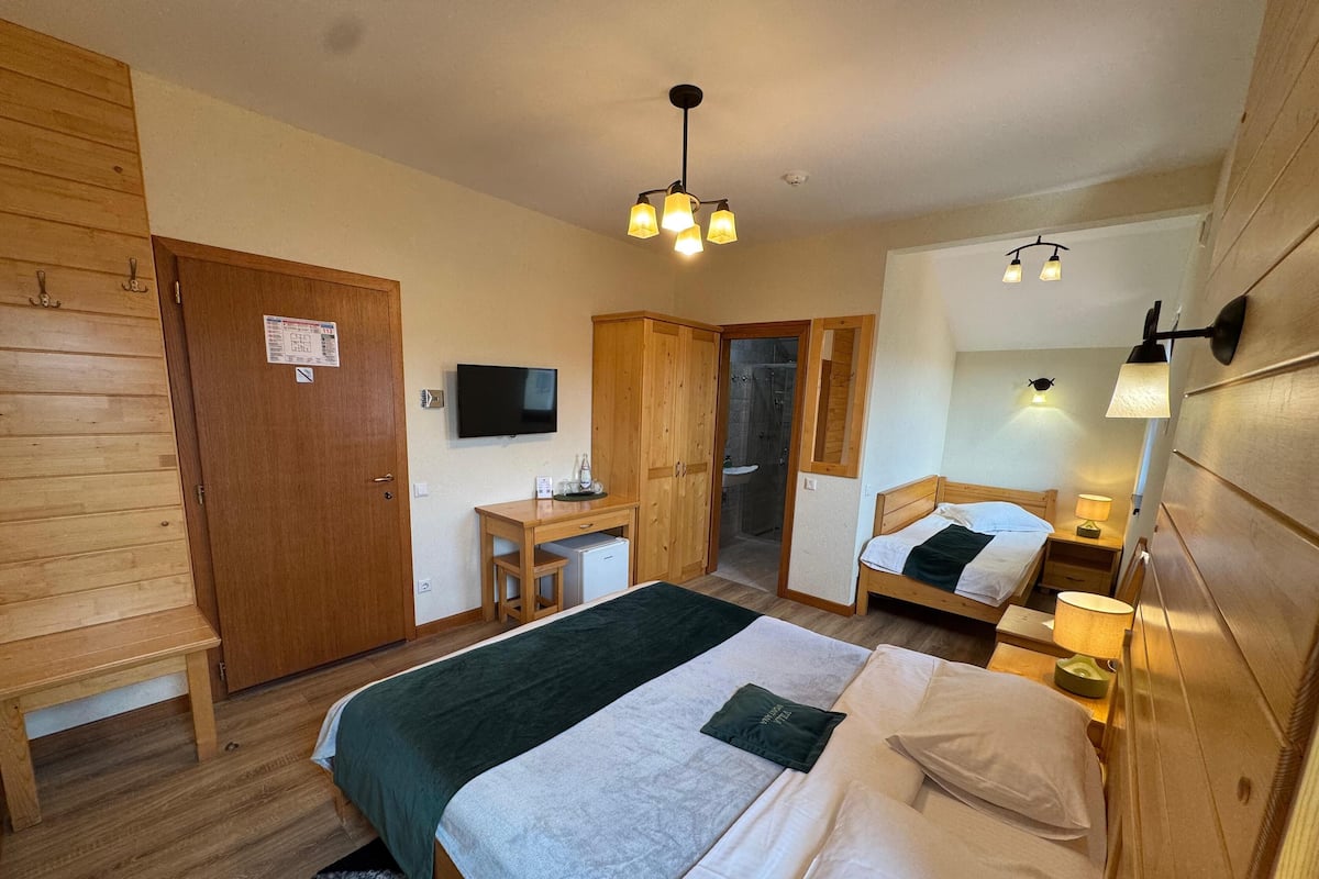 A bedroom with a bed, bedside tables, a desk, a mirror, and a shower area.