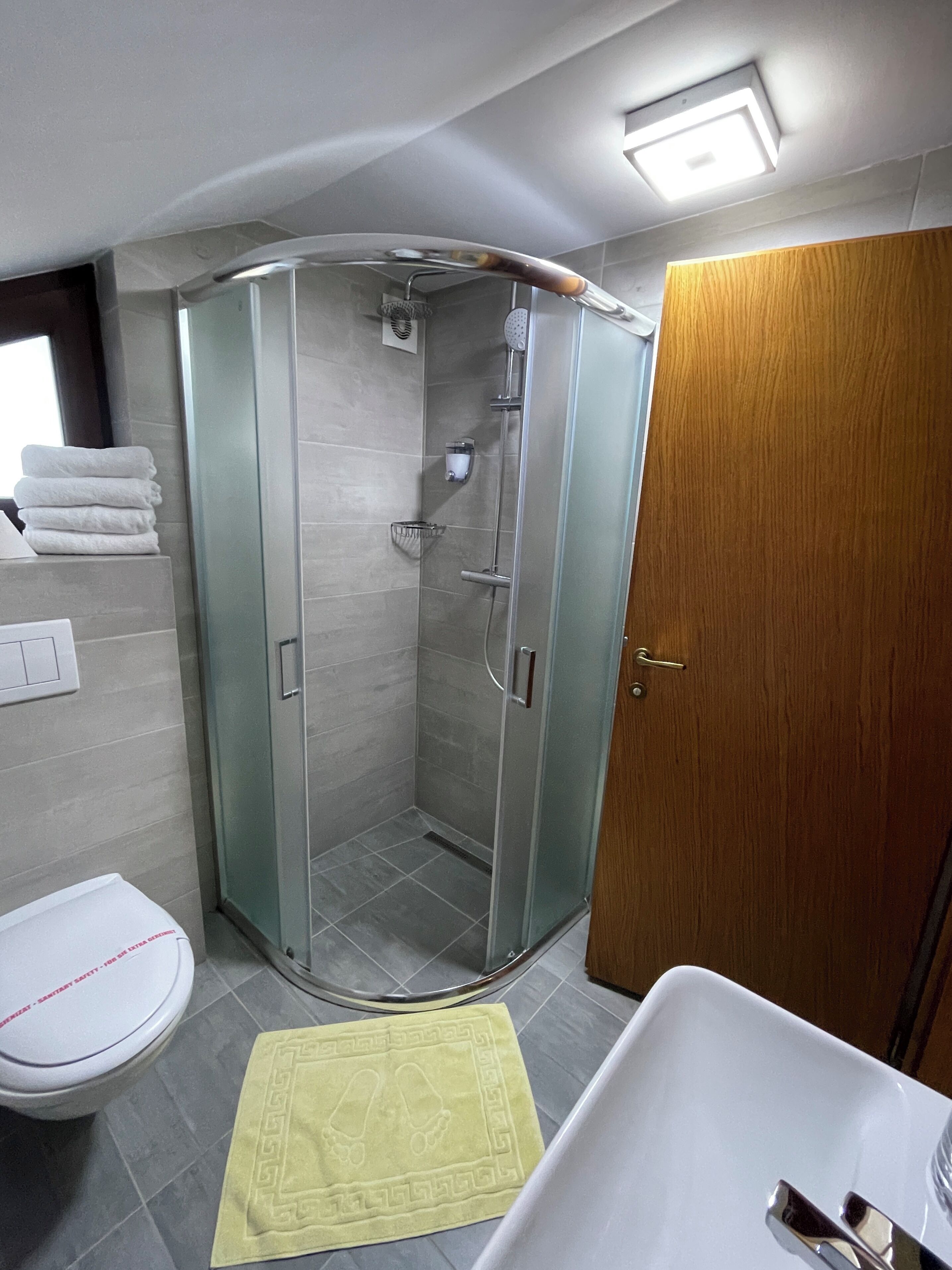 A modern bathroom with a glass-enclosed shower, a white sink, and a wooden door.