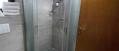 A modern bathroom with a glass-enclosed shower, a white sink, and a wooden door.