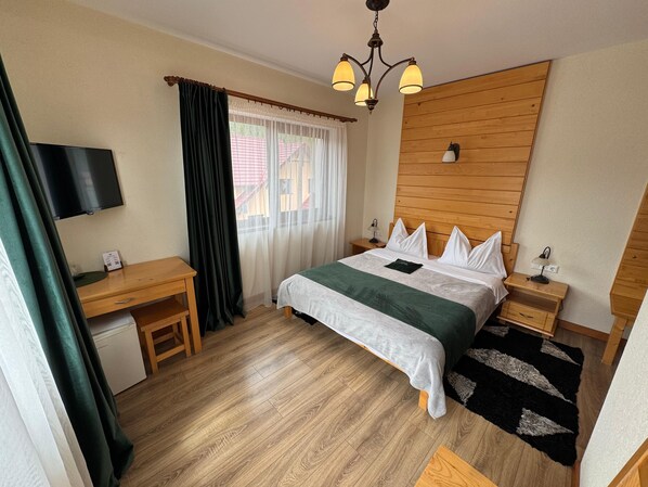 A hotel room with a wooden bed, a desk, a chair, a TV, and a window with curtains. - Villa Montana (Borsec)