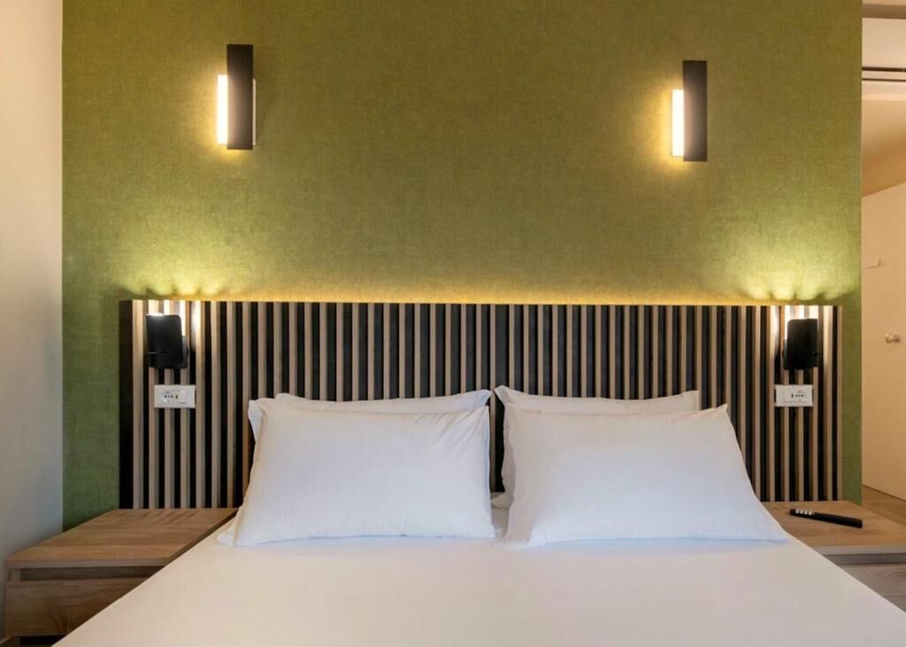 A neatly made bed with white linens and two pillows, flanked by two wall-mounted nightstands with black lamps.