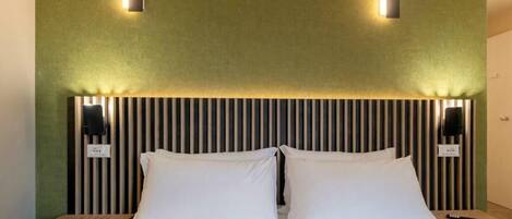 A neatly made bed with white linens and two pillows, flanked by two wall-mounted nightstands with black lamps.