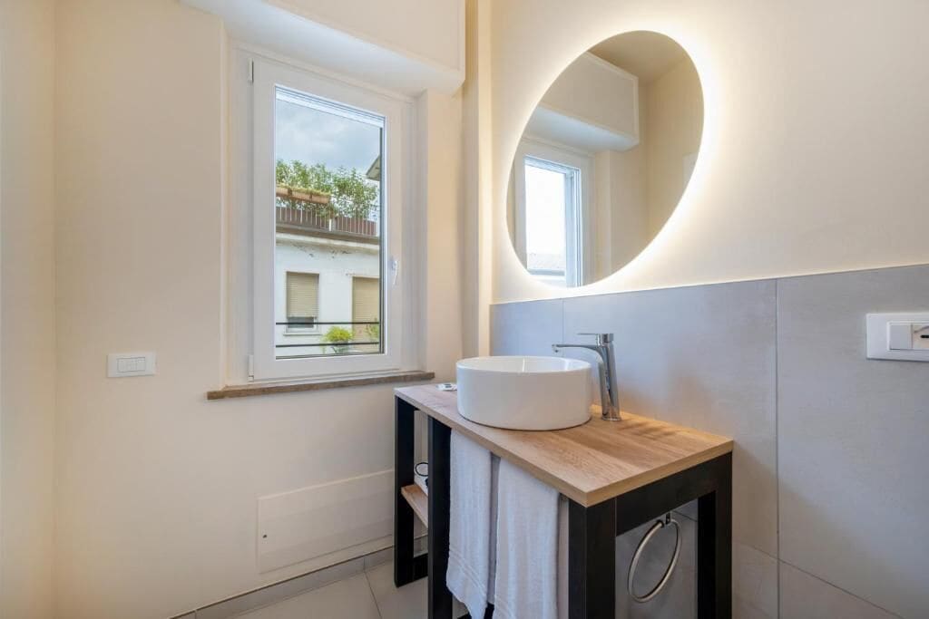 A modern bathroom with a round mirror, a vessel sink, and a window.