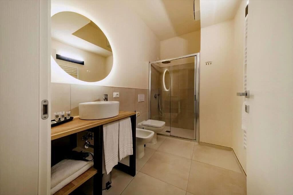 A modern bathroom with a round mirror, a sink, a toilet, and a shower.
