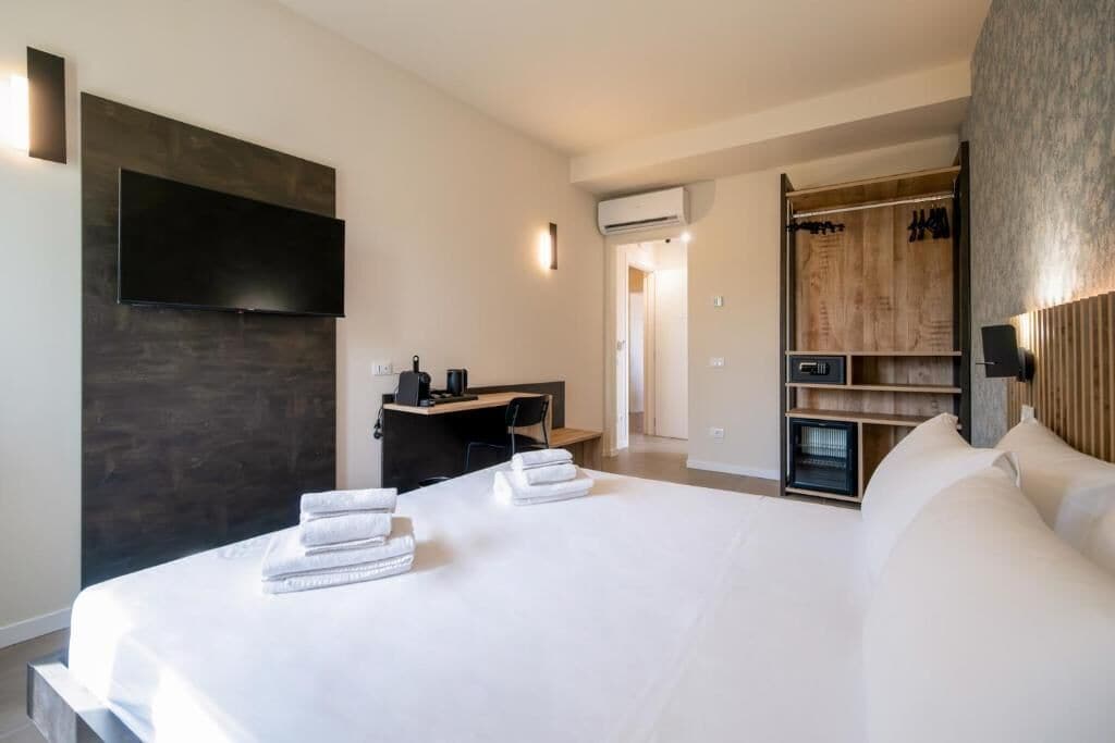 Una camera d'albergo moderna con un letto grande, una scrivania con una sedia, una TV a schermo piatto montata a parete e un armadio con scaffali.