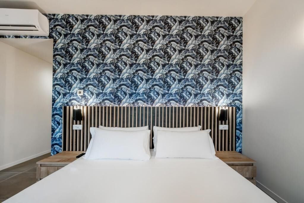 Habitación de hotel con cama, dos mesitas de noche, cabecero con listones verticales y papel tapiz estampado.