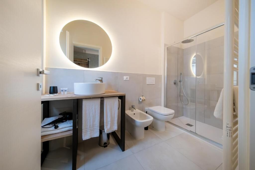 Un baño moderno con un espejo redondo, un lavamanos, un bidé y una ducha con mampara de vidrio.