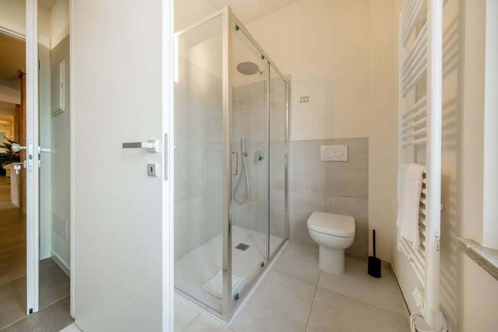 A modern bathroom with a glass-enclosed shower, a toilet, and a radiator.