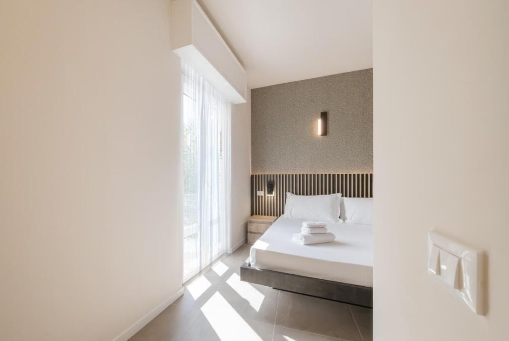 A modern hotel room with a large bed, a nightstand, and a wall-mounted light fixture.