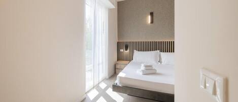 A modern hotel room with a large bed, a nightstand, and a wall-mounted light fixture.