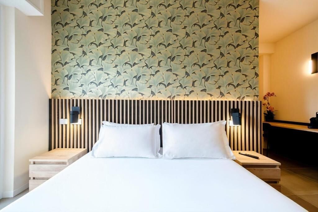 A hotel room with a bed, two bedside tables, a wall with a leaf pattern, and a wooden headboard.