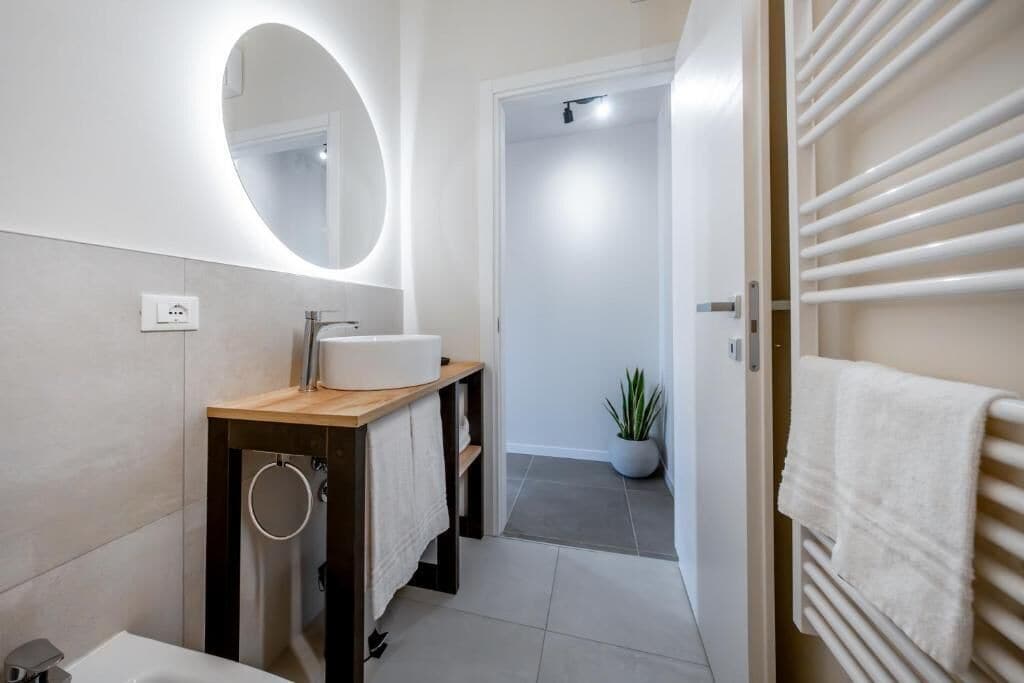 Une salle de bain moderne avec un meuble-lavabo en bois, un miroir rond, un lavabo blanc et un porte-serviettes.