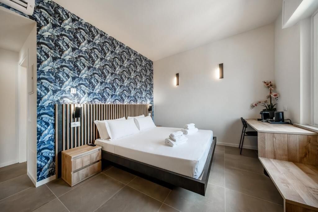 A modern hotel room with a large bed, a desk, and a wall with a leaf pattern.