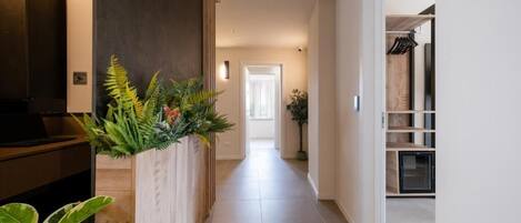A hallway with a wooden cabinet on the left, a plant, and a door at the end.