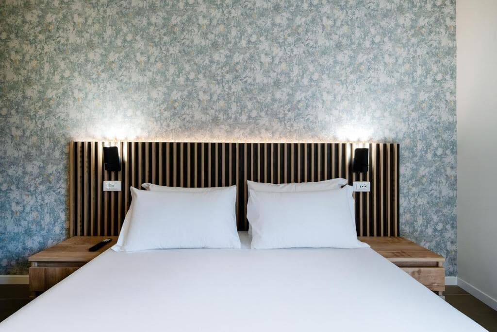 Un lit bien fait, avec du linge de lit blanc, deux tables de chevet avec des lampes et une tête de lit à lattes verticales.