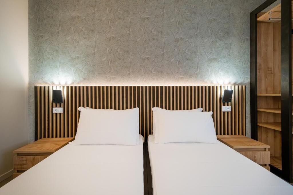 Ein Doppelbett mit weißen Laken, zwei Nachttische und eine Wand mit vertikalen Holzleisten.