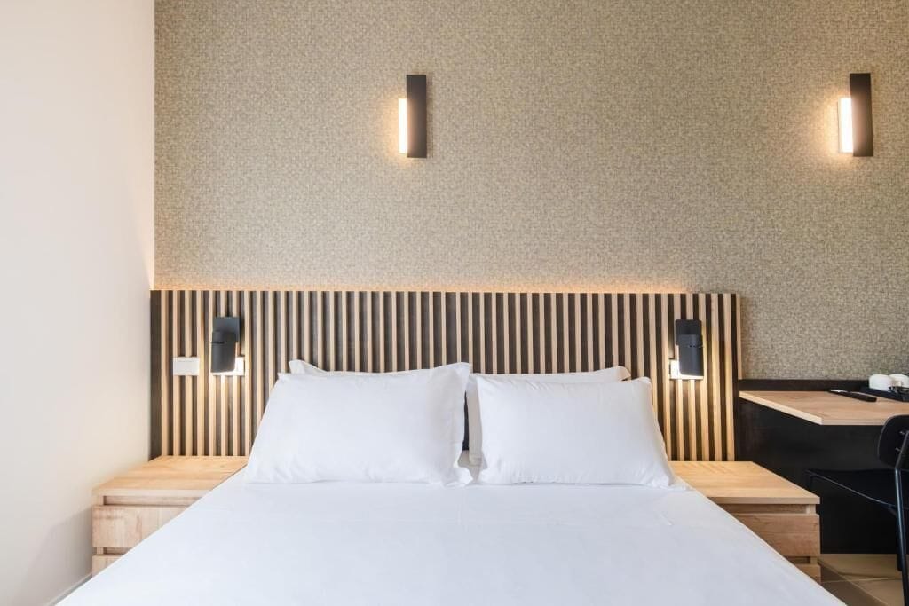 Habitació d'hotel moderna amb un llit gran, un panell de fusta al capçal, dues taules de nit i un escriptori petit amb una cadira.