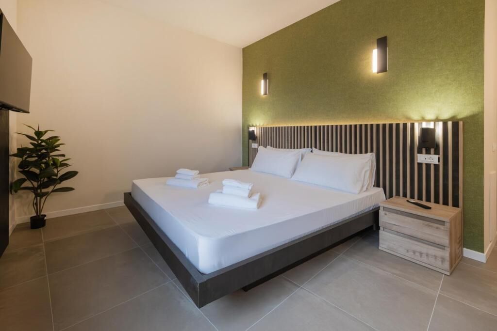 Ett modernt hotellrum med en stor säng, ett sängbord, ett litet bord och en krukväxt.