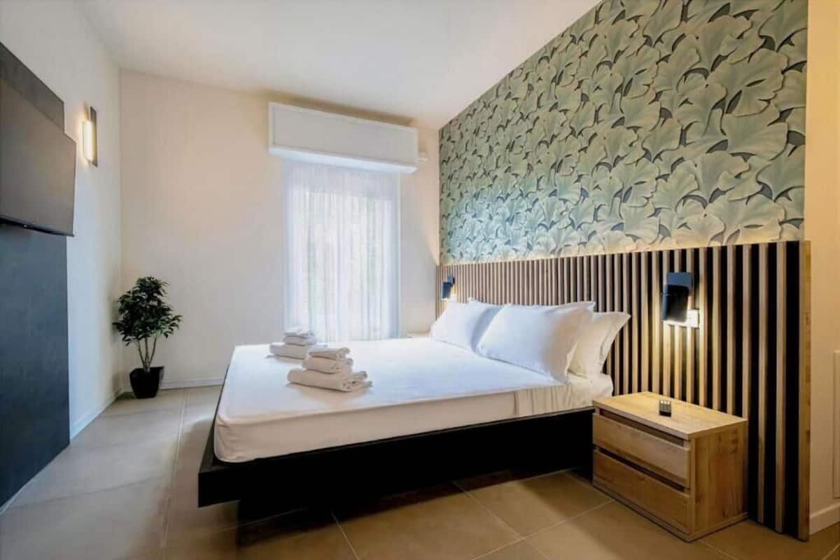 Una habitación de hotel moderna con cama, mesita de noche y un panel decorativo en la pared.