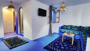 A modern living room with a blue sofa, two hanging lamps, a flat-screen TV, and a patterned rug.