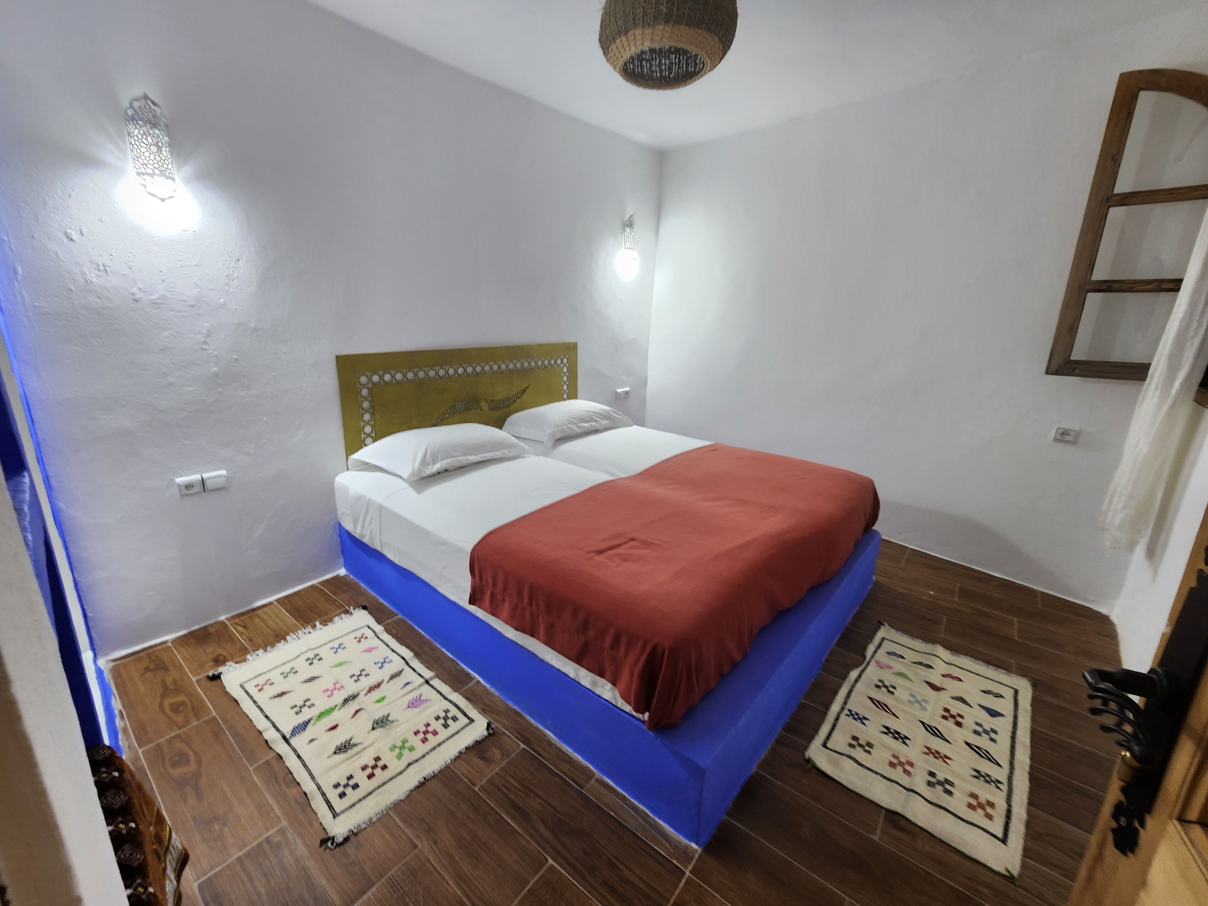 A bedroom with a bed, white walls, a wooden headboard, and a red blanket.