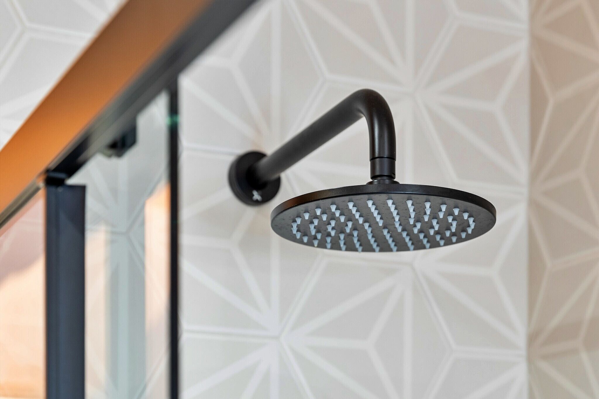 A modern showerhead with a curved handle, mounted on a wall with a geometric pattern.