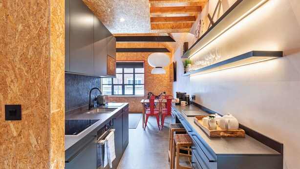 A modern kitchen with a wooden ceiling, a large window, and a dining area with red chairs.