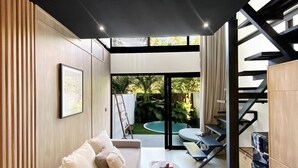 Una sala de estar moderna con un sofá, una mesita y una escalera que lleva a un área exterior con piscina.