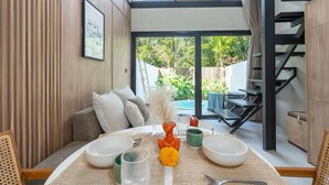 Un comedor con una mesa dispuesta para dos personas, una escalera y una piscina al fondo.