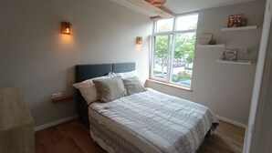 Un dormitorio con cama, ventana y estante con libros.
