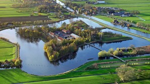 Un río serpentea por un paisaje rural con campos y un pequeño grupo de edificios cerca del agua.