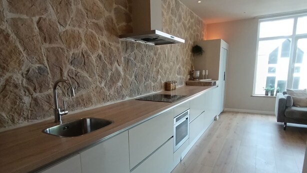 Una cocina moderna con pared de piedra, encimera de madera y electrodomésticos integrados.