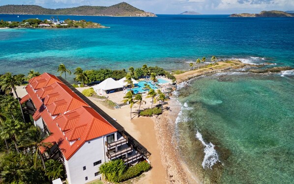 A coastal hotel with a red-roofed building, a pool area, and clear turquoise waters.